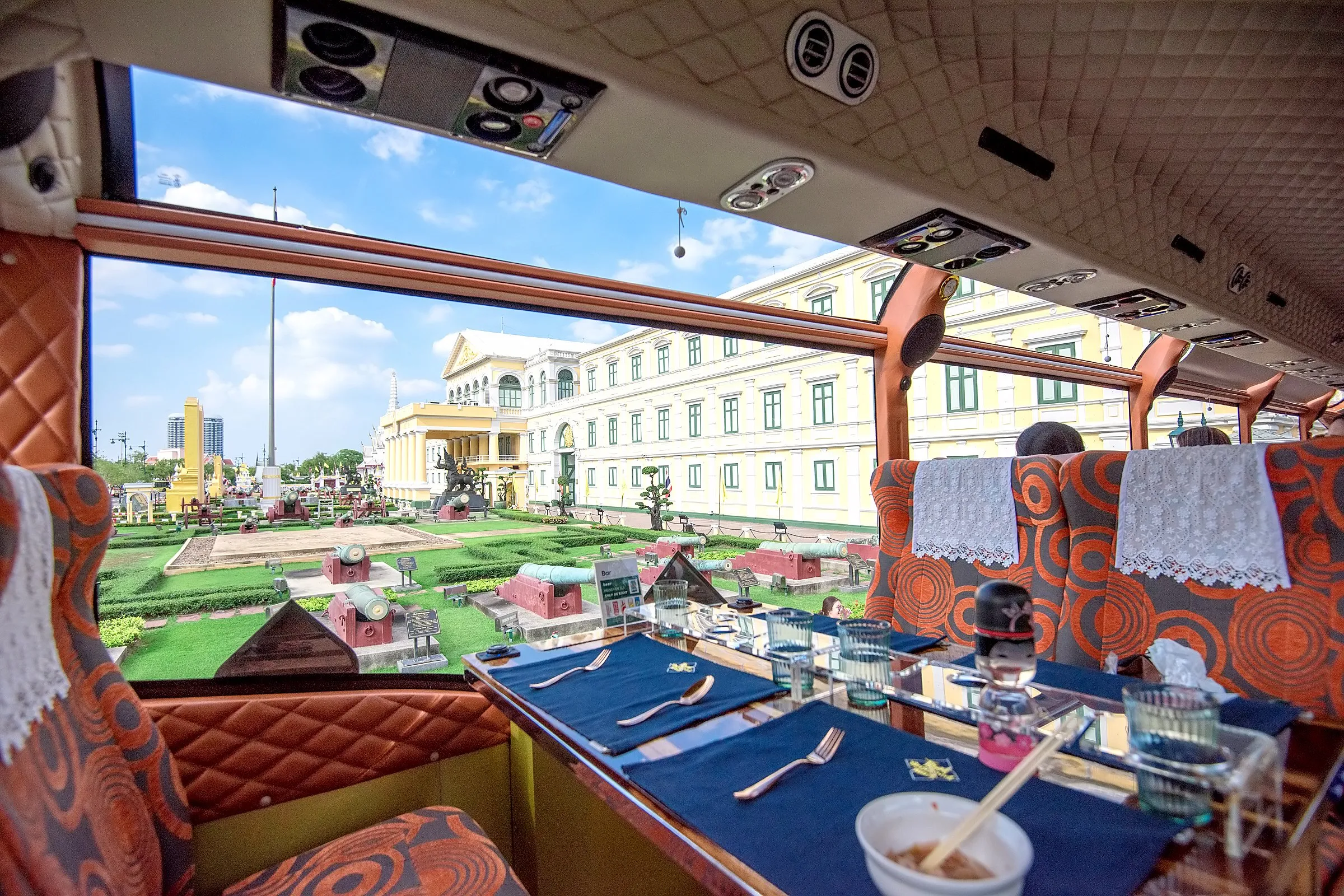 Afternoon tea served on a table aboard the Thai Bus Food Tour double-decker with Bangkok Old Town landmarks visible through the window