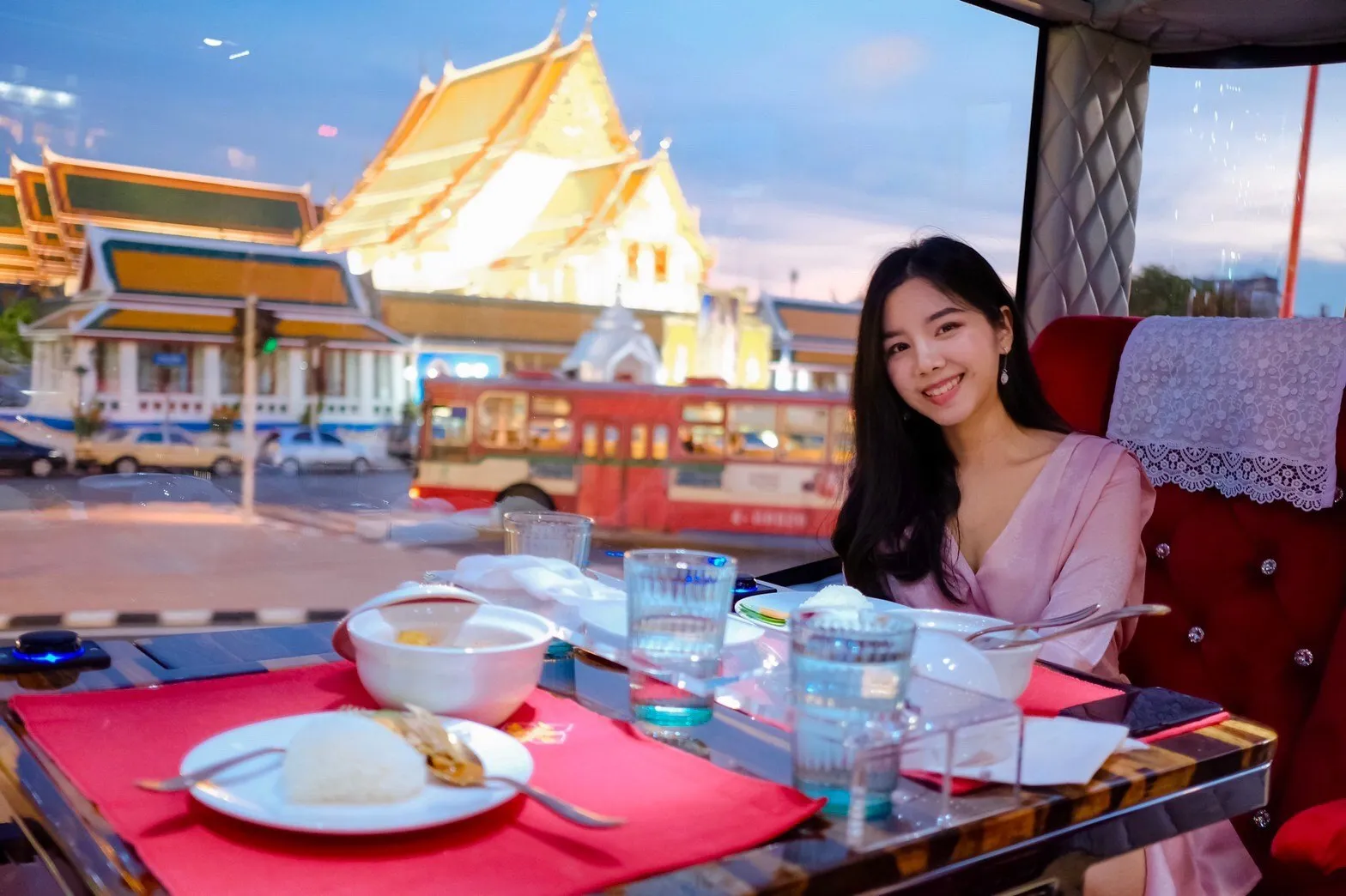 Intimate sunset dinner aboard the luxury bus with a golden Bangkok temple glowing beyond the window